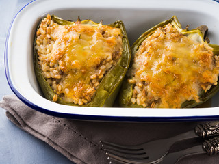 Bell peppers stuffed with mixed cereals, meat and cheese baked in enamel tin on blue
