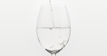 pouring water into wine glass over white background