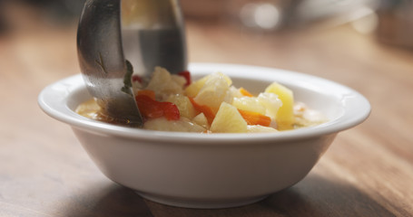closeup pouring cauliflower soup into bowl on wood table