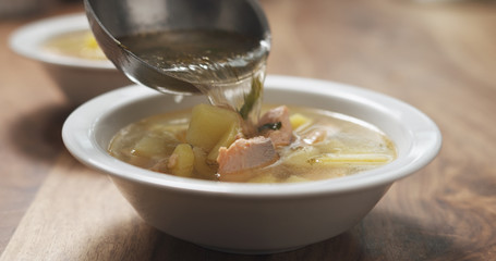 closeup pour fish soup with salmon into bowl