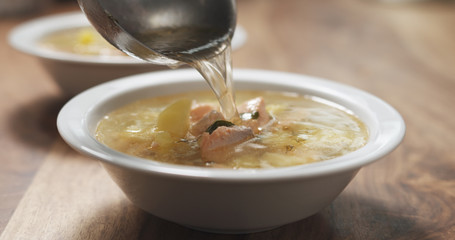 closeup pour fish soup with salmon into bowl
