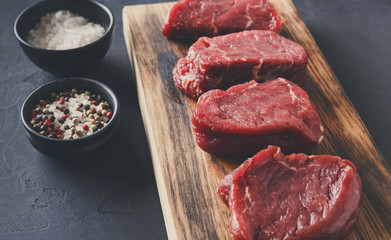 Raw beef filet mignon steaks with spices on wooden board at blac