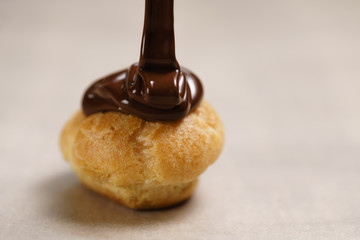 pouring dark chocolate on profiterole on parchment paper