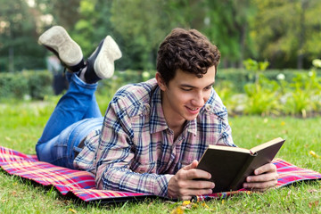 young men student lying  in the park with the book in his hands