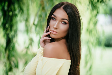 young beautiful brunette woman posing in yellow elegance dress at green summer park 