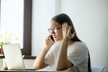 Young frustrated businesswoman discussing contract details over the phone. Female freelancer solves problems by phone.