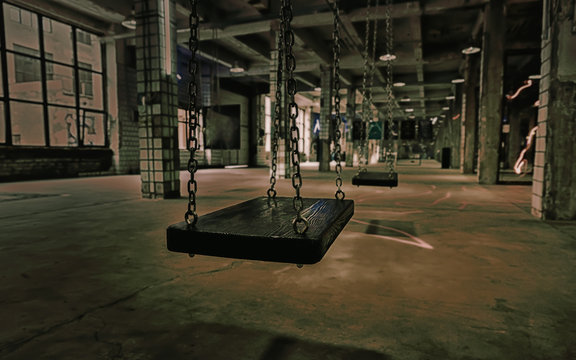 Swings in an abandoned old gloomy building with breakaway tiles on the walls