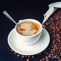 Coffee cup with a spoon and coffee beans on table.