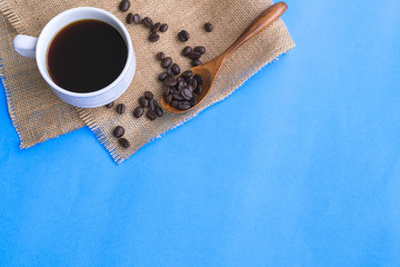 A cup of coffee and coffee bean grain on sack fabric put on blue background include copyspace for add text or graphic
