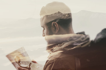 Photo of stylish bearded traveler with a compass and map in hand. Double exposure, beautiful mountain landscape background. Made in vintage style.