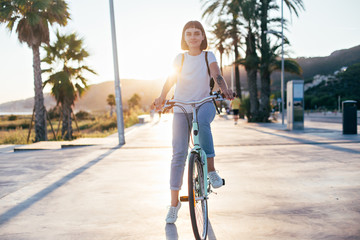Happy beautiful hipster millennial woman or teenager with cool arm tattoos, is tourist in summer of spain or italy, she rides rental cruiser bicycle, happy and relaxed enjoying youth and freedom