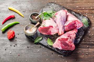 Raw lamb shanks with salt and pepper on stone tray on rustic wooden table, selective focus