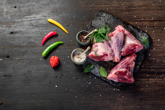 Raw lamb shanks with salt and pepper on stone tray on rustic wooden table, selective focus