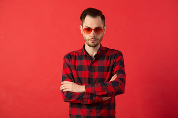 portrait of a stylish young guy in a checkered shirt and wearing red glasses on a red background