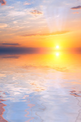 Sunset and rays in the sky with sunlit clouds above the sea.