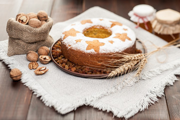homemade traditional fruit cake on clay plate decorated with wheat ears, nuts and honey jars at wooden table