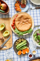 Above view image of delicious food on table over checkered tablecloth: freshly baked pie surrounded by fruits, vegetables and salad