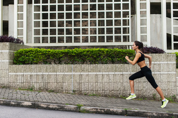Fototapeta na wymiar Side view of young female runner listening to music and jogging on sidewalk in town