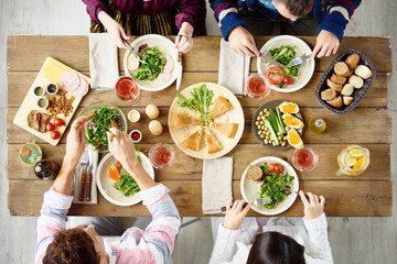 Top view of four people eating at festive dinner table with delicious food in cafe or restaurant