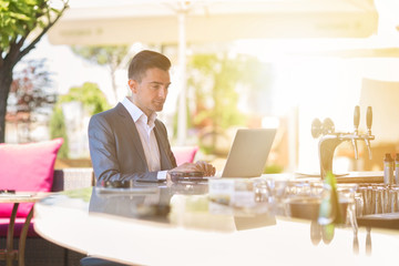 Handsome young businessman is sitting at the bar and working on a laptop