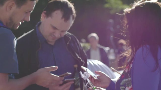 Happy friends watching photos on a smartphone in the park on a sunny day with lens flare effects in slow motion. 3840x2160