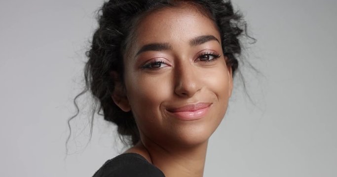 Close up slow motion video of a young girl with perfect light brown skin and beautiful curly black hair smiling at the camera on white background.