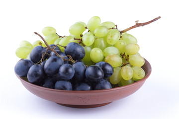 Green and blue grapes in a clay plate on a white background
