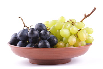 Green and blue grapes in a clay plate on a white background