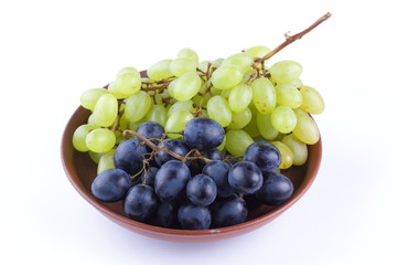 Green and blue grapes in a clay plate on a white background