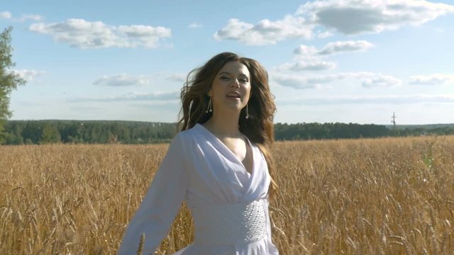 A singer in a white dress is singing on a field with wheat.