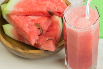 Watermelon juice in a glass glass with a straw on a light wooden background, a cocktail, a plate with slices of ripe berries watermelon