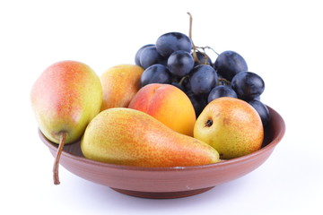 Yellow pears, green and blue grapes in a clay plate on a white background