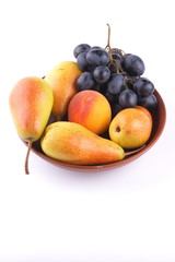 Yellow pears, green and blue grapes in a clay plate on a white background