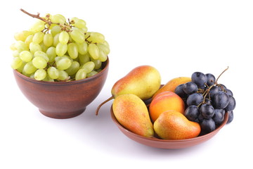 Yellow pears, green and blue grapes in a clay plate on a white background