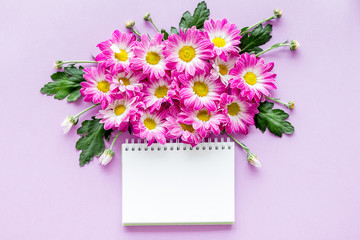 Floral mockup. Notebook near pink flowers on purple background top view