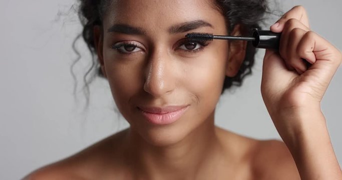 Adorable teenage Middle Eastern girl with great skin applying mascara to her long lashes on white background