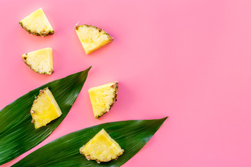 Tropical fruits background. Pinneapple slices in front of big leaves on pink background top view copyspace