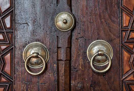 Closeup of two antique copper ornate door knockers over an aged wooden door