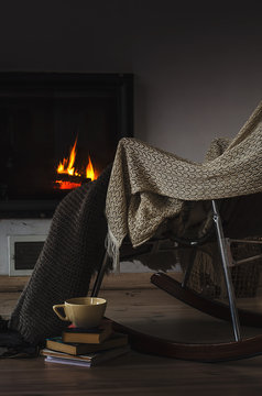 Rocking chair with knit rug, books and cup of tea or coffee before fireplace