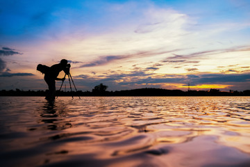 Silhouette of a photographer, taking the beautiful moments during the sunset at have water reflection light.