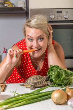 Tortoise eating roman salad while young woman bites carrot