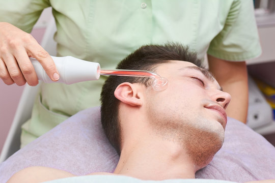 Skin treatment with darsonval device. Young caucasian man, beauty clinic. Stimulating collagen production.
