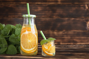 bottles of water with citrus (orange and lemon) on a wooden table on a background of mint