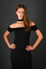 Young brunette lady in black dress posing on grey background