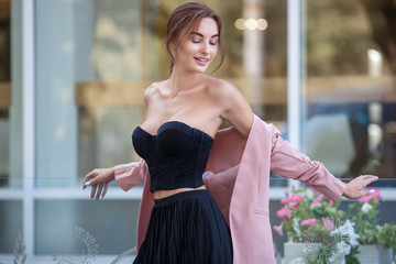Naklejka premium Young and fresh beautiful woman with naked shoulders in pleated skirt and pink jacket outside.