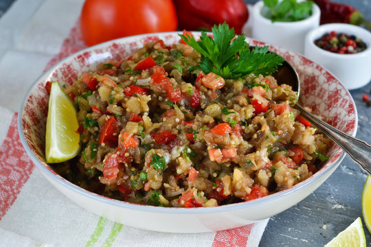 Snack salad of roasted eggplant with garlic and tomato on a concrete background