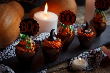 Halloween Cucpcakes with text topper decoration and orange cream. Candles and pumpkin background