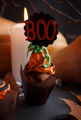Halloween Cucpcakes with text topper decoration and orange cream. Candles and pumpkin background