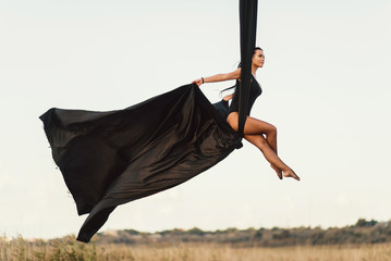 Elegance young beautiful woman dance with aerial silk on a sky background. Fly yoga sport 