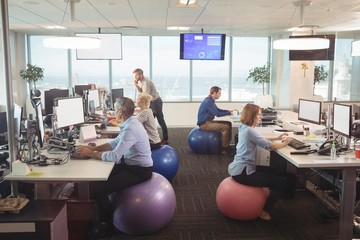 Business people working at desk while sitting on exercise balls - Powered by Adobe